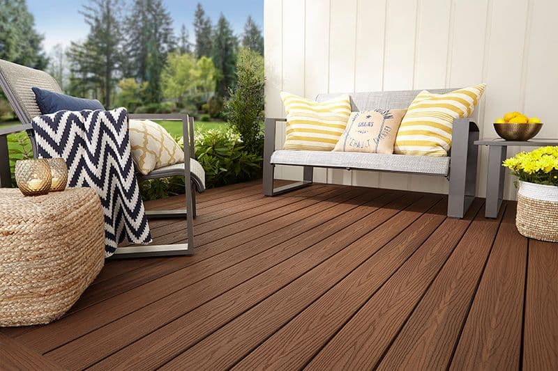 Terrasse med moderne hagemøbler med fargerike puter og brune terrassebord.