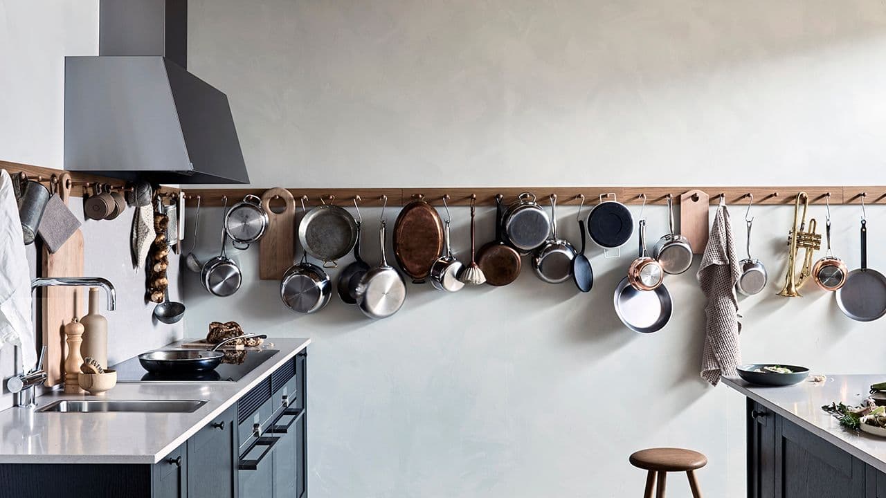 Svart kjøkkenvifte som matcher kjøkkenet i et landlig kjøkken med lang knaggrekke til kjøkkenredskaper.