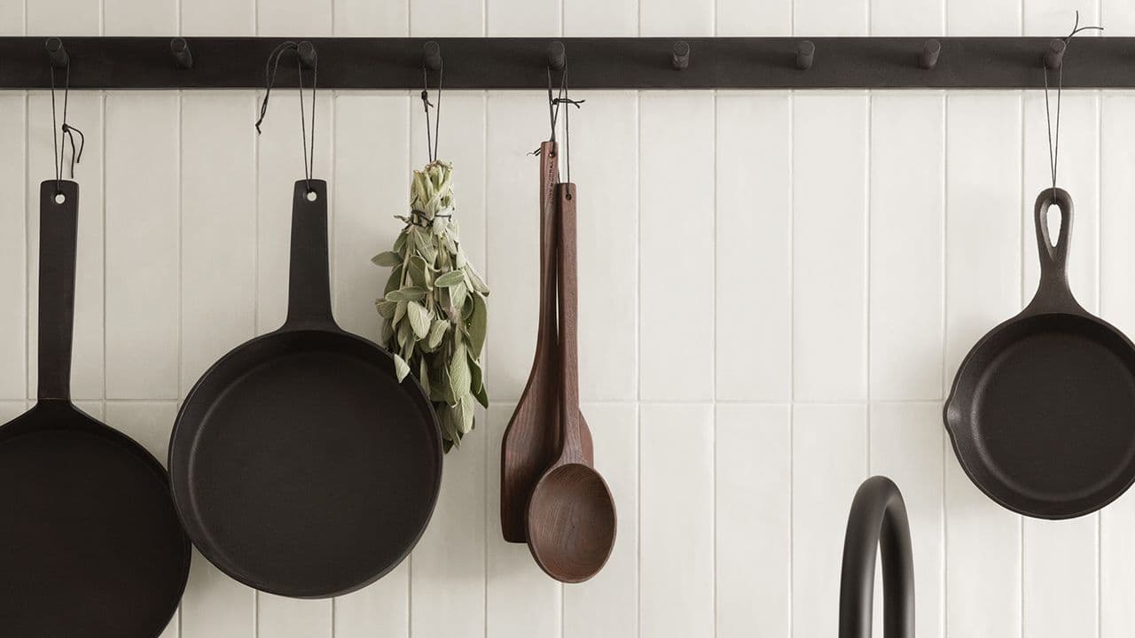 Svart knaggrekke med jernstekepanner hengende i landlig kjøkken.