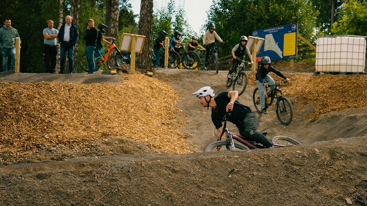 Flere gutter som sykler i sykkelpark mens det står folk å ser på.