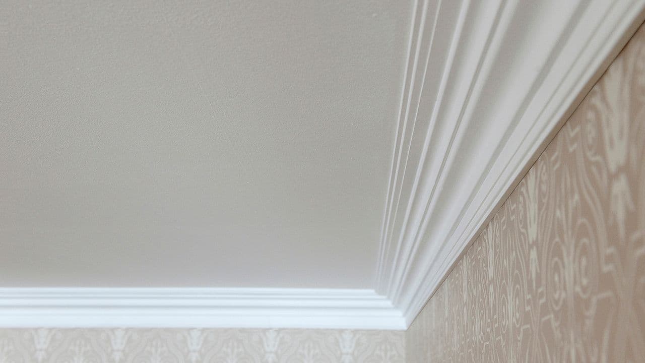 Profilerte lister i taket til vegg med mønstret tapet.