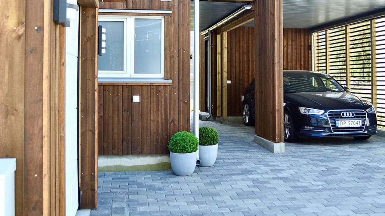Belegningsstein på gårdsplass og en bil parkert i carport.