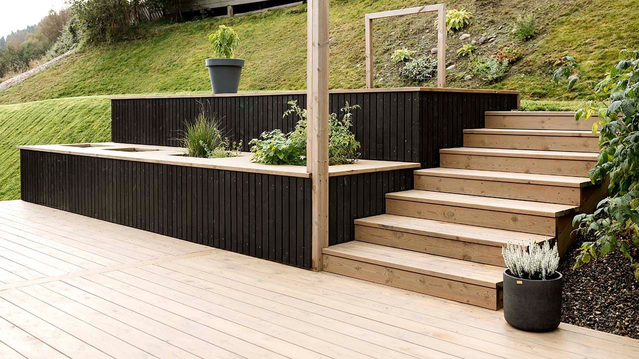 Trykkimpregnerte terrassebord på terrasse med plantekasser bygget i skråning med trapp.